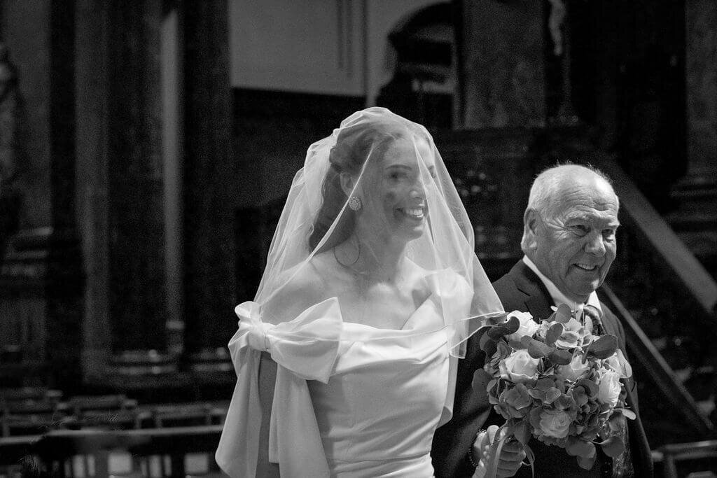 Bride holding fathers arm walking down aisle at Brompton Oratory London