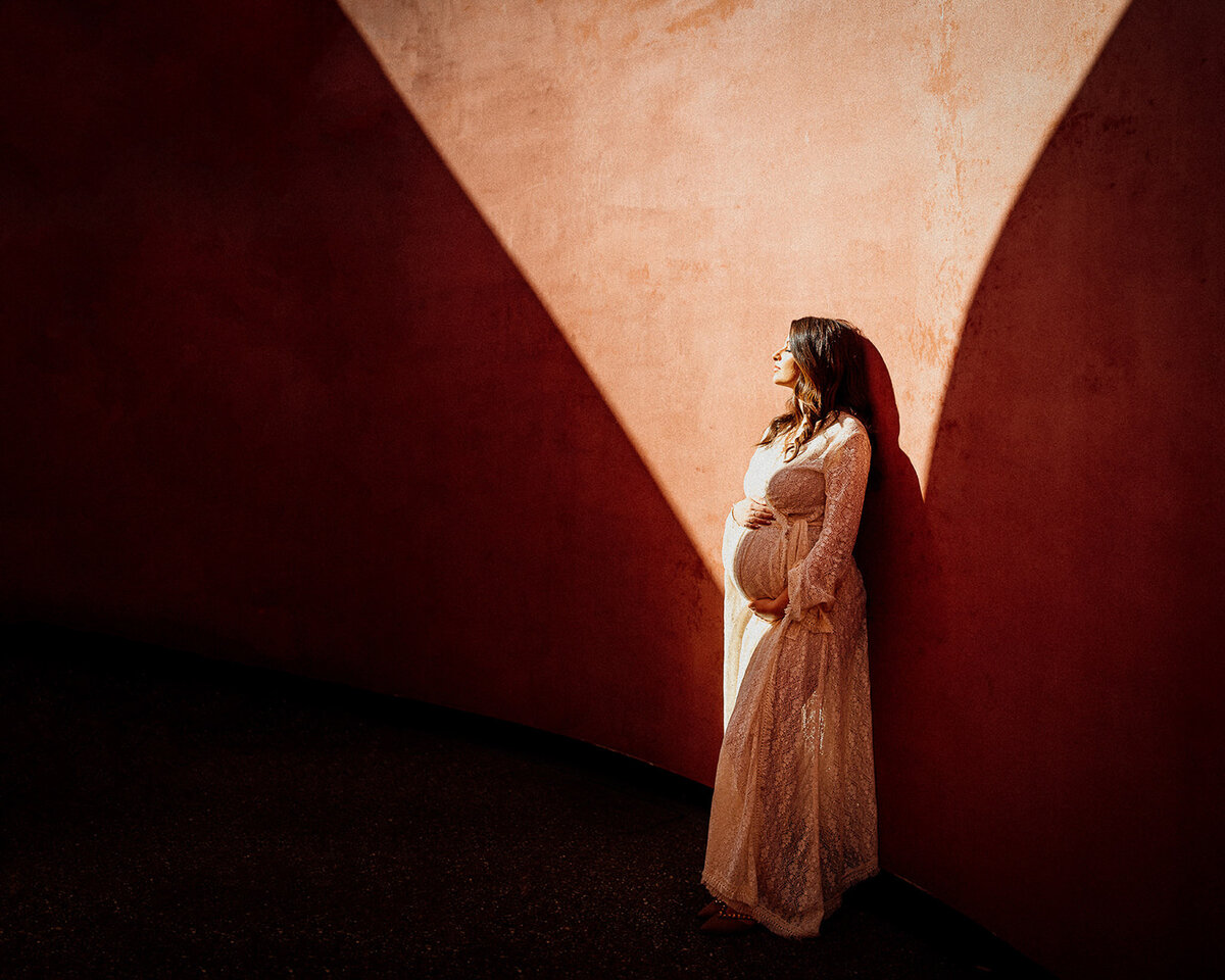 Bay area maternity portrait at the de young museum, Women bathed in sunlight with shadow lines on terracotta walls