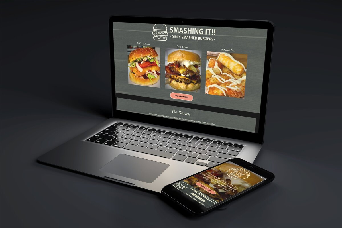 A laptop and smartphone displaying the "Smashing It!!" website, featuring mouth-watering images of dirty smashed burgers. The screen shows a variety of burgers, including the "Halloumi Burger," "Dirty Burger," and "Halloumi Fries," with a call-to-action button to view the full menu. The devices are placed on a dark surface, emphasizing the vibrant and appetising food images.