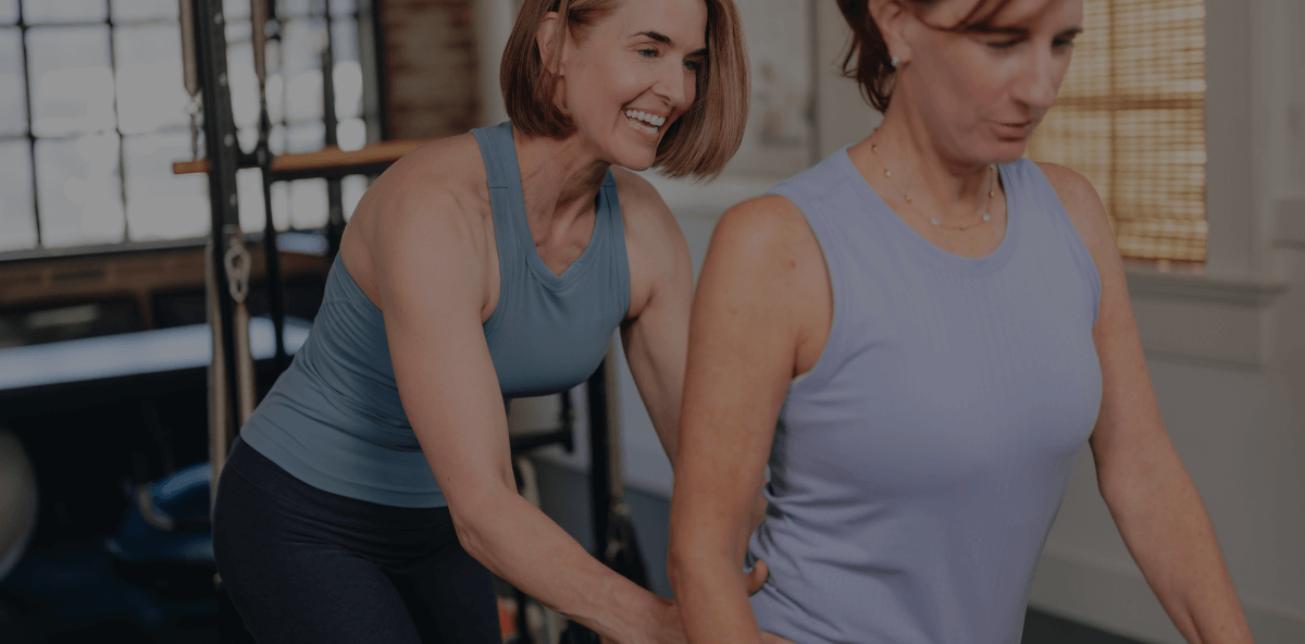 PIlates Mentors lead instructor assisting a woman in a blue tank on a reformer 