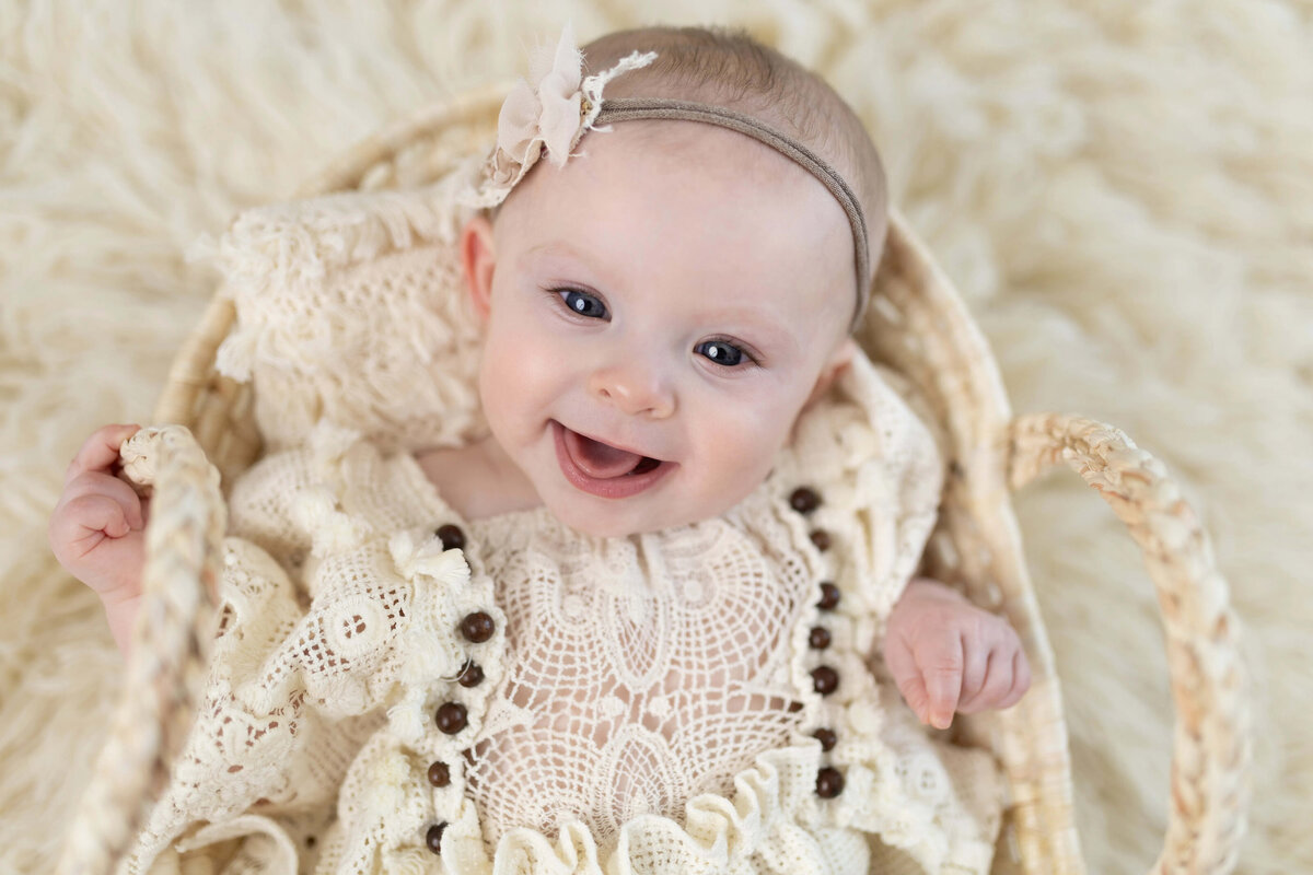 Smiling baby girl in lace outfit lying in basket - milestone session Maple Grove photographer 