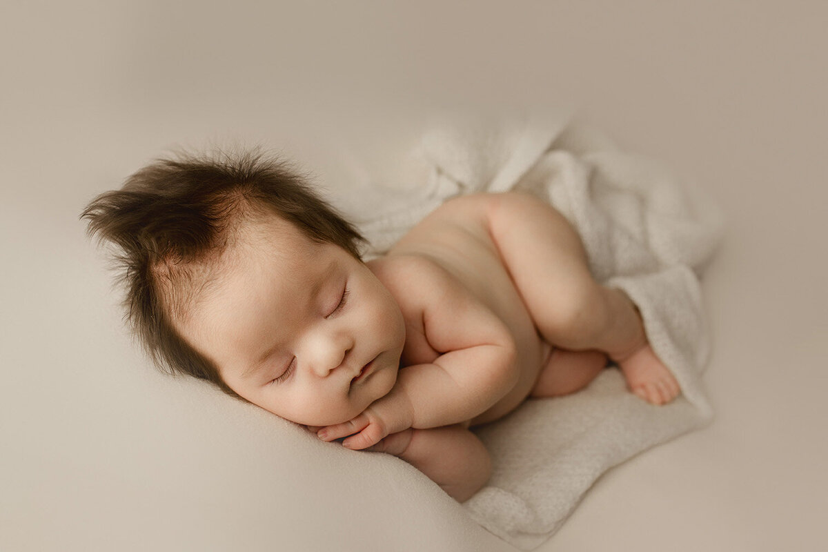 A newborn boy with a full head of hair lays on his side in rochester, ny