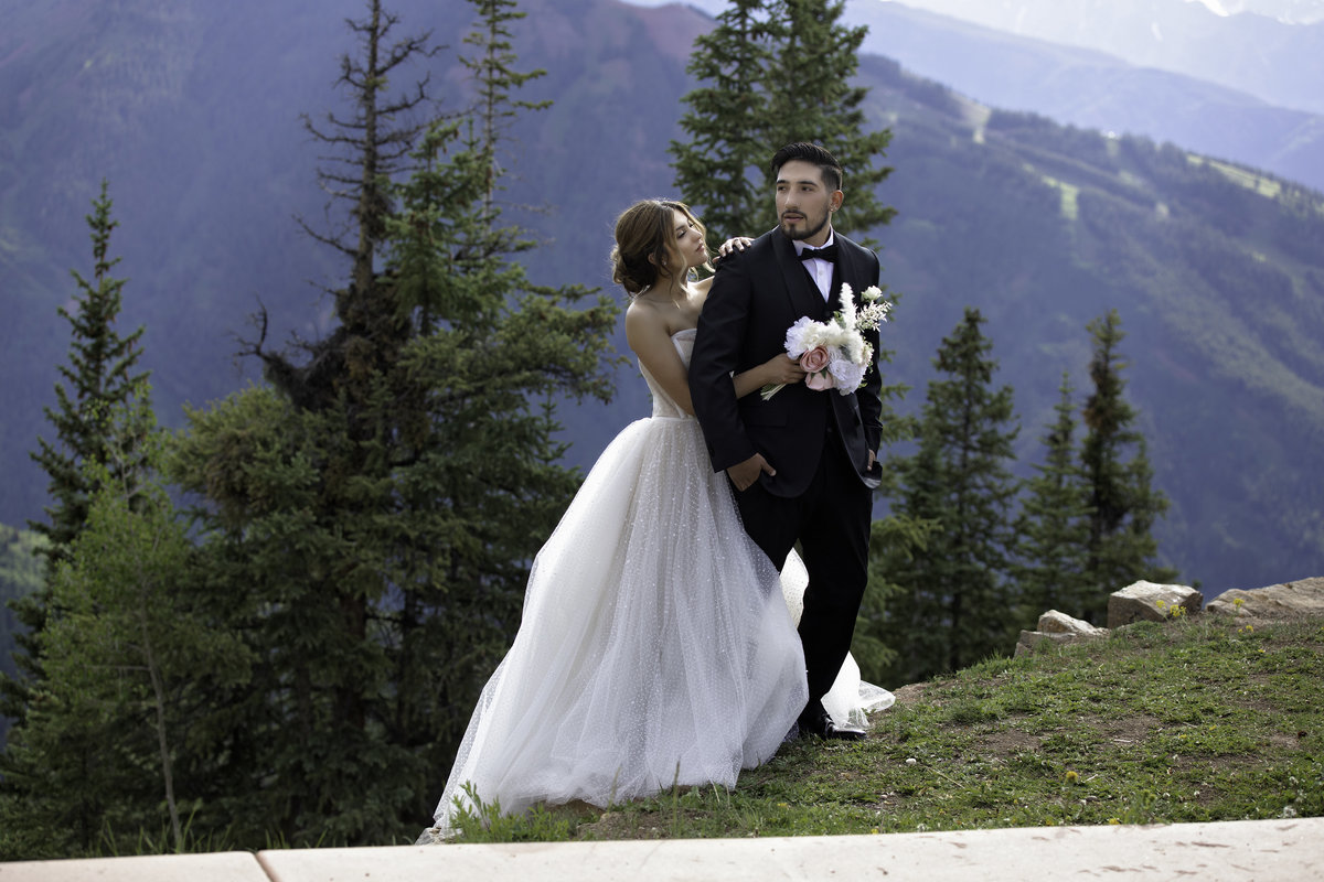 Bride embraces groom from behind as they stand in front of a beautiful mountain
