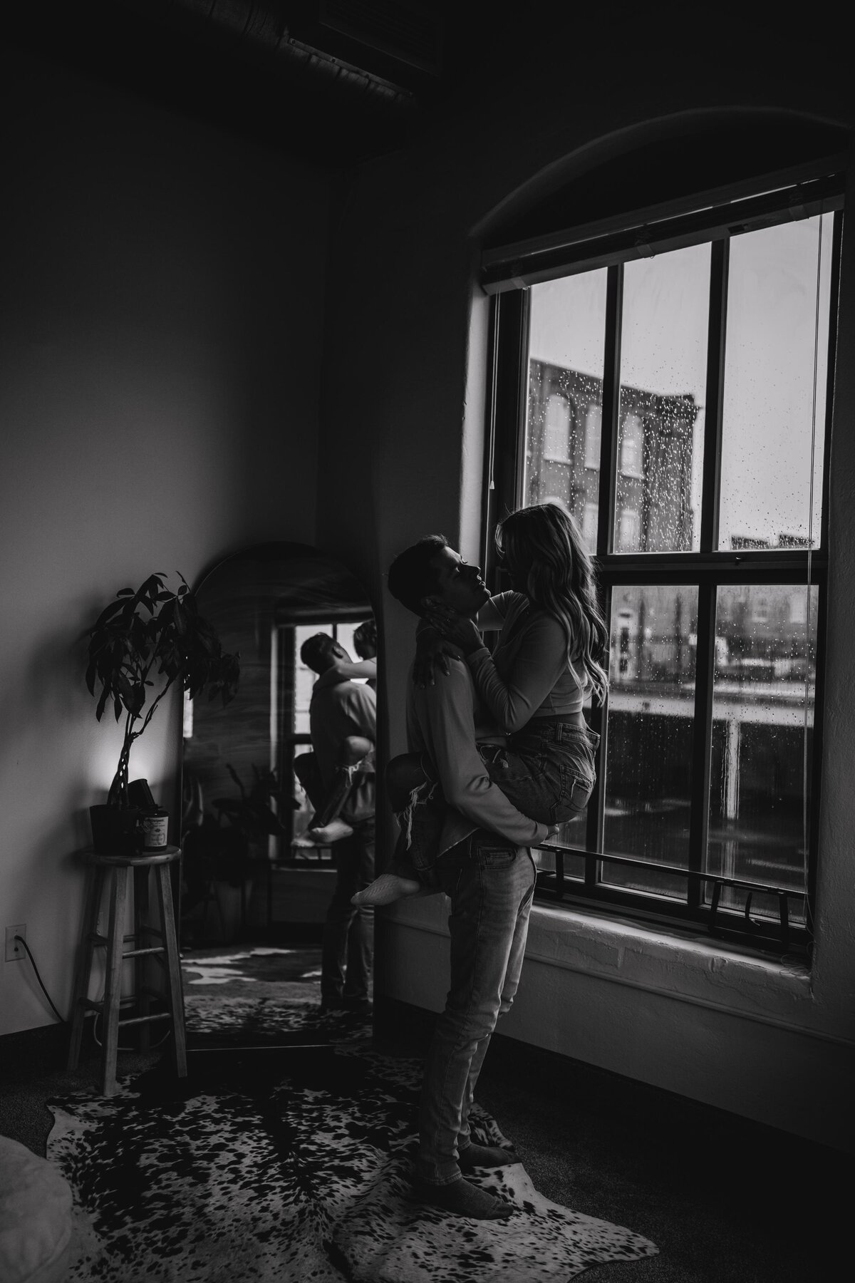 Black & white editorial-style couples session in a cozy, moody Pittsburgh loft, featuring intimate moments by a rainy window.