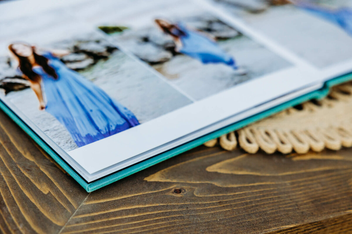 image of the gorgeous details from a high school senior photo album that shows the bright teal color of the cover and thick pages as it sits on a wooden table