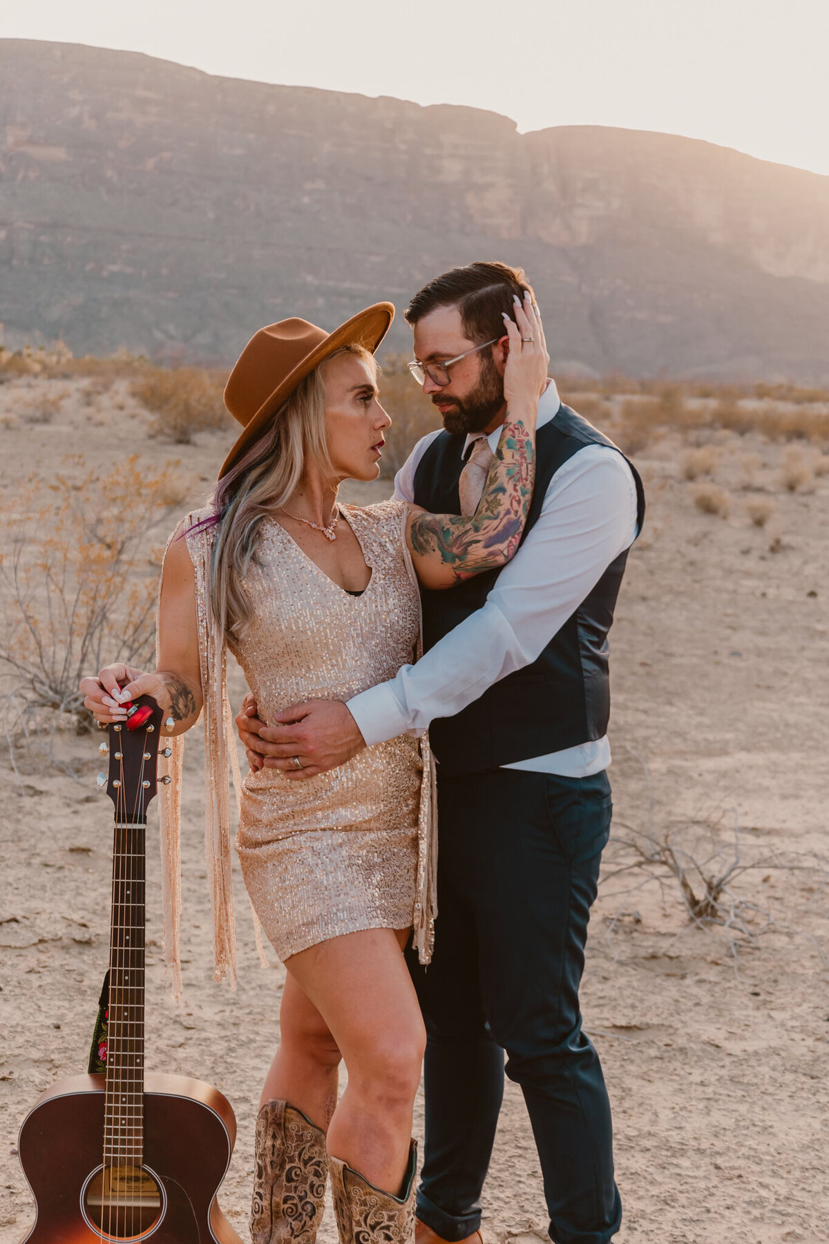 Romantic couple portrait at Big Bend State Park during a creative elopement session. The woman wears a sparkling dress and hat, holding a guitar, while the man embraces her lovingly. Captured by ShutterUp Photography.