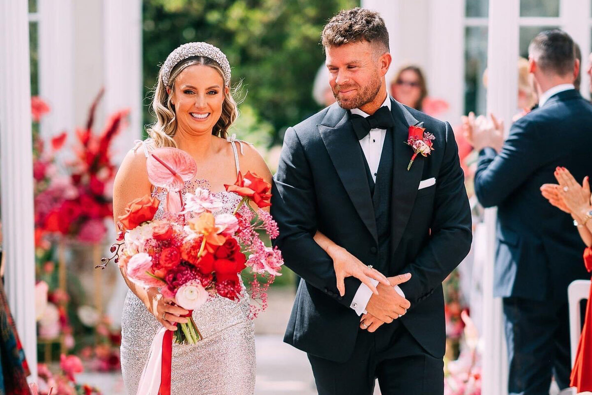 Bride with pink and orange bouquet running with groom through lawn