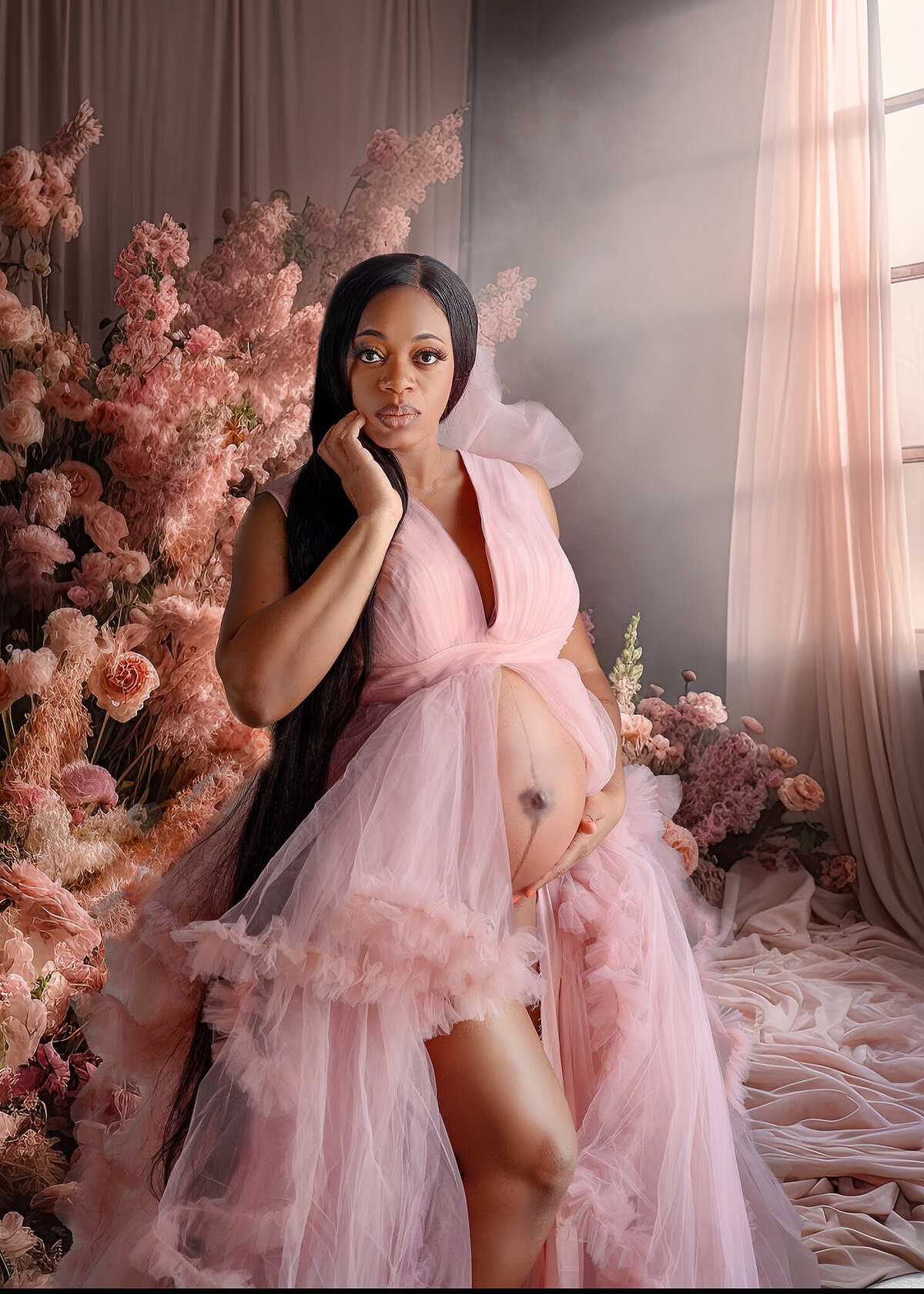 Beautiful Nigerian pregnant woman , wearing a soft pink tulle gown, posing in a room with pink fabrics, flowers and large window letting in lots of beautiful light