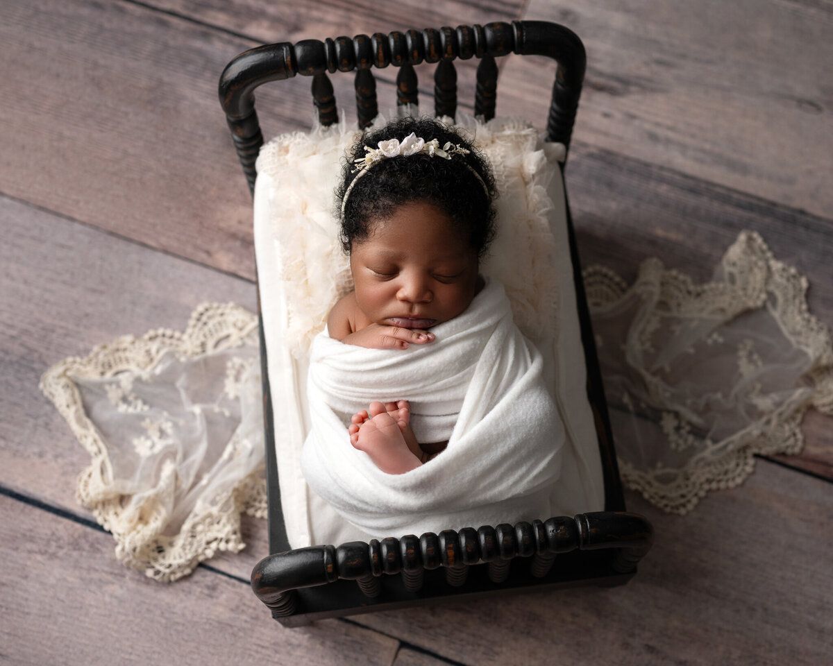 newborn baby girl wrapped in white swaddle sleeping on a black bed with lace accents