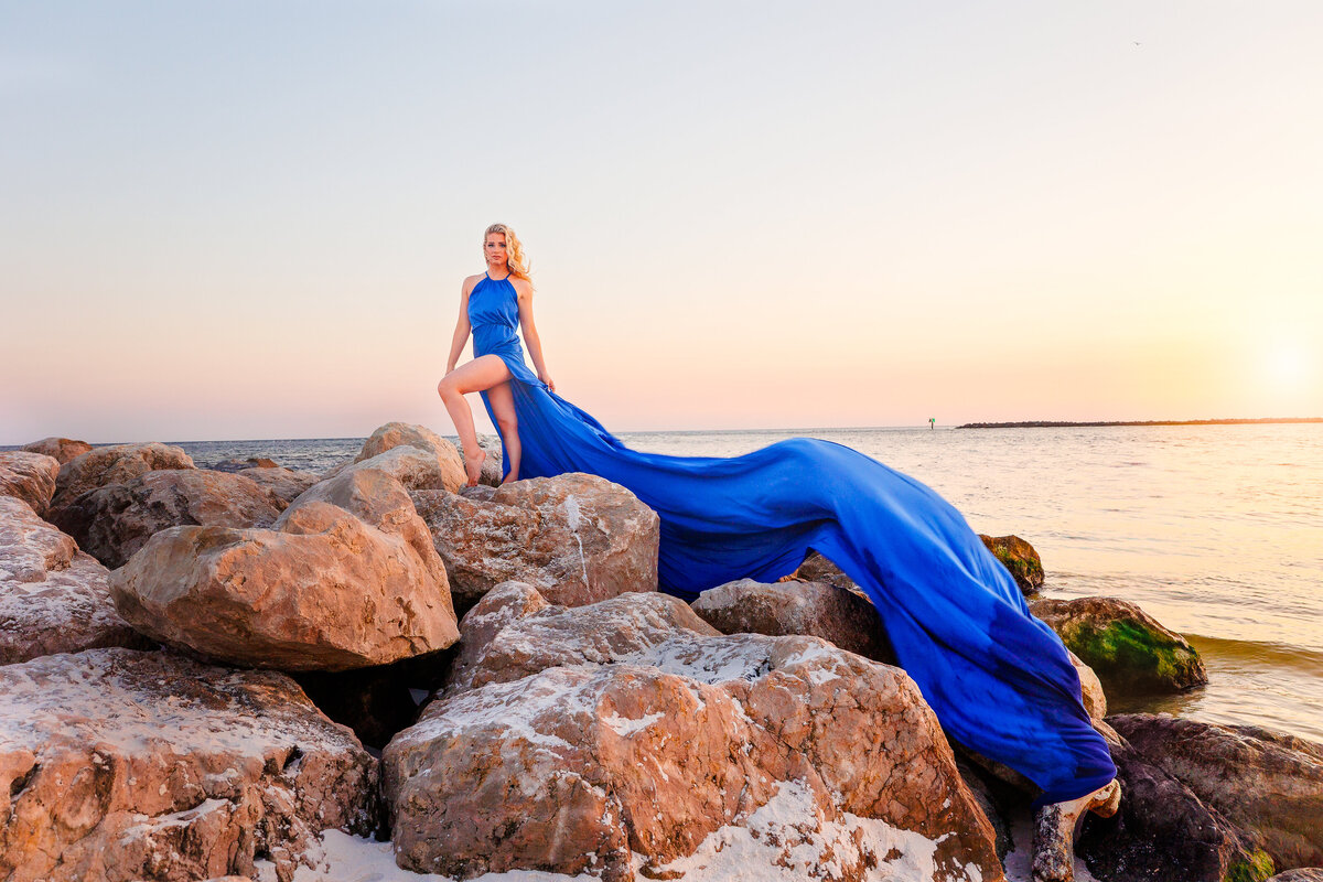 Girl standing on rocks in Orange Beach Alabama wearing a cobalt blue dress flying dress