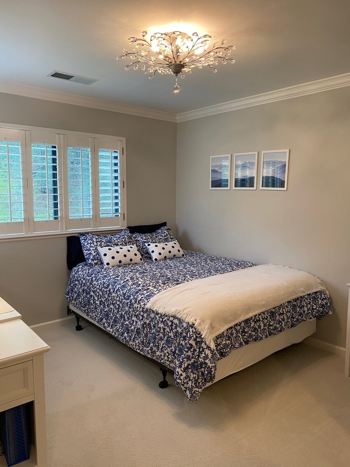 A bright, updated bedroom with soft neutral walls, crown molding, plantation shutters, and a modern decorative ceiling light, remodeled by an East Bay home improvement contractor.