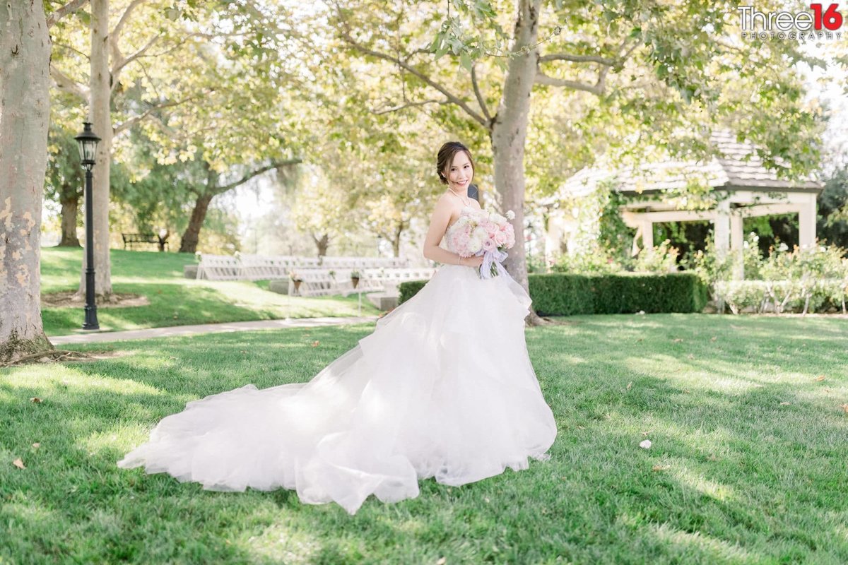 Beautiful Bride poses with her dress train fanned out on the lawn