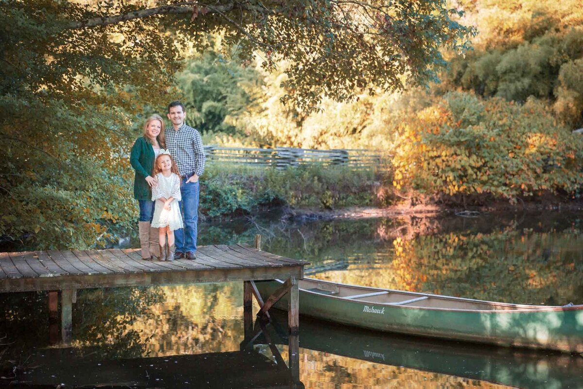 A gorgeous family portrait on the dock at a pond with a canoe on a beautiful fall day.
