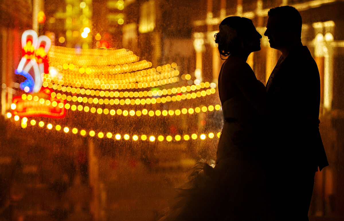 A couple is silhouetted as lights behind them stretch across a street.