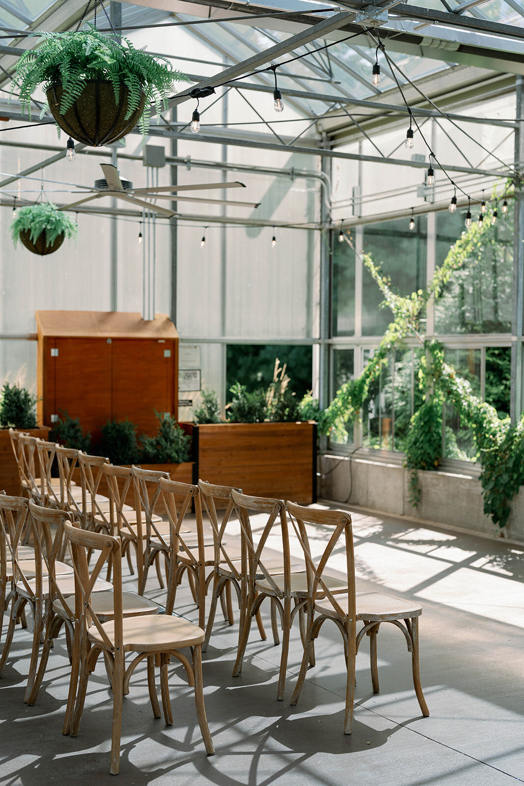 Styled empty ceremony view showing chairs, greenery and aisle décor inside The Ivy House greenhouse.