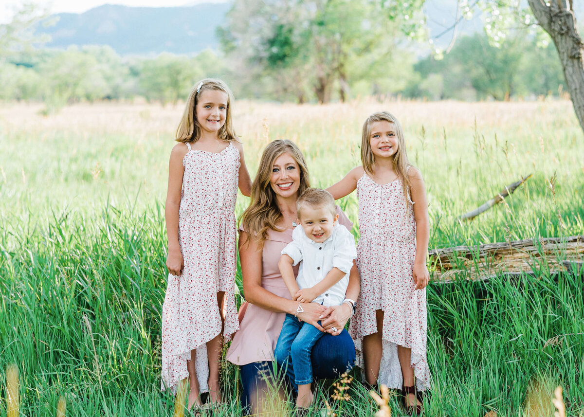 A blonde mom wearing pink and blue pose with her children in a green and grassy field