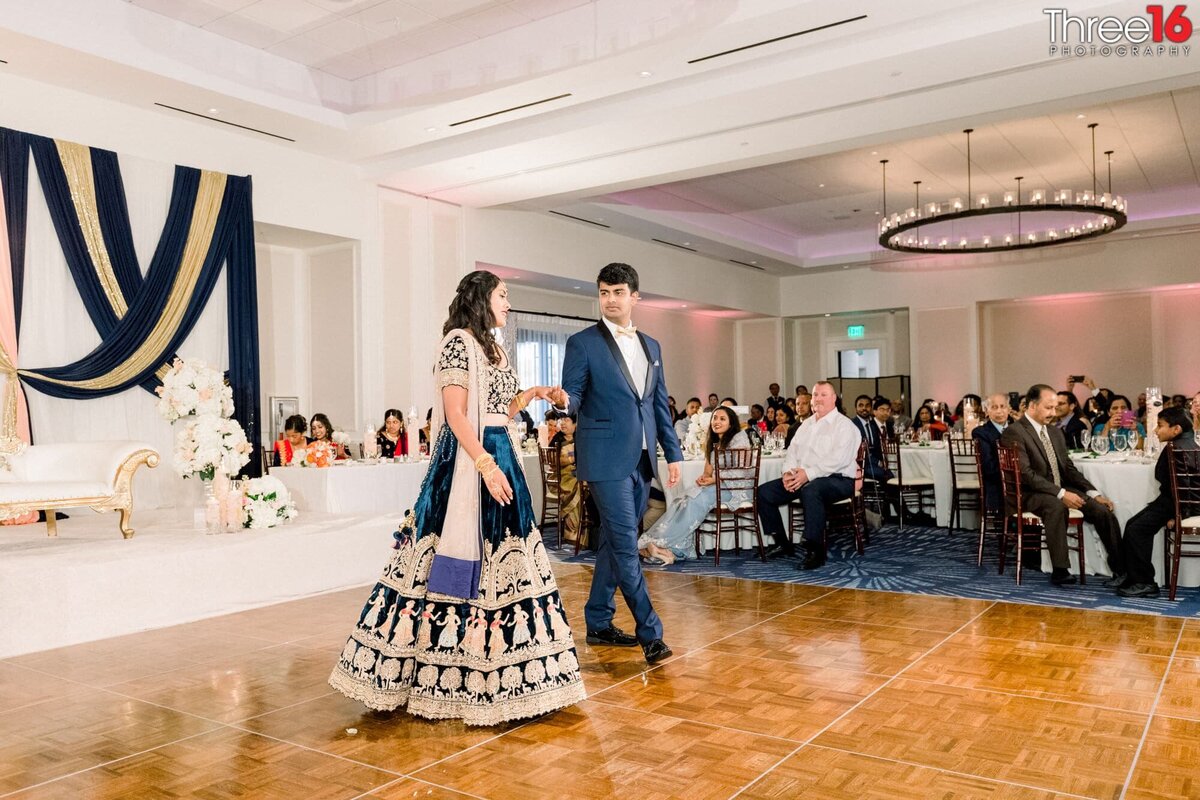 Bride and Groom walk out onto the dance floor holding hands in traditional Indian wedding attire