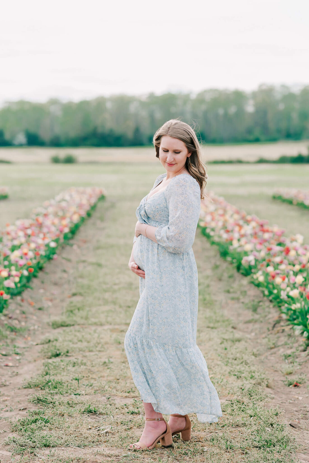Expecting mom in a pale blue floral dress holding her bum at Burnside Farms, by a nothern virginia maternity photographer