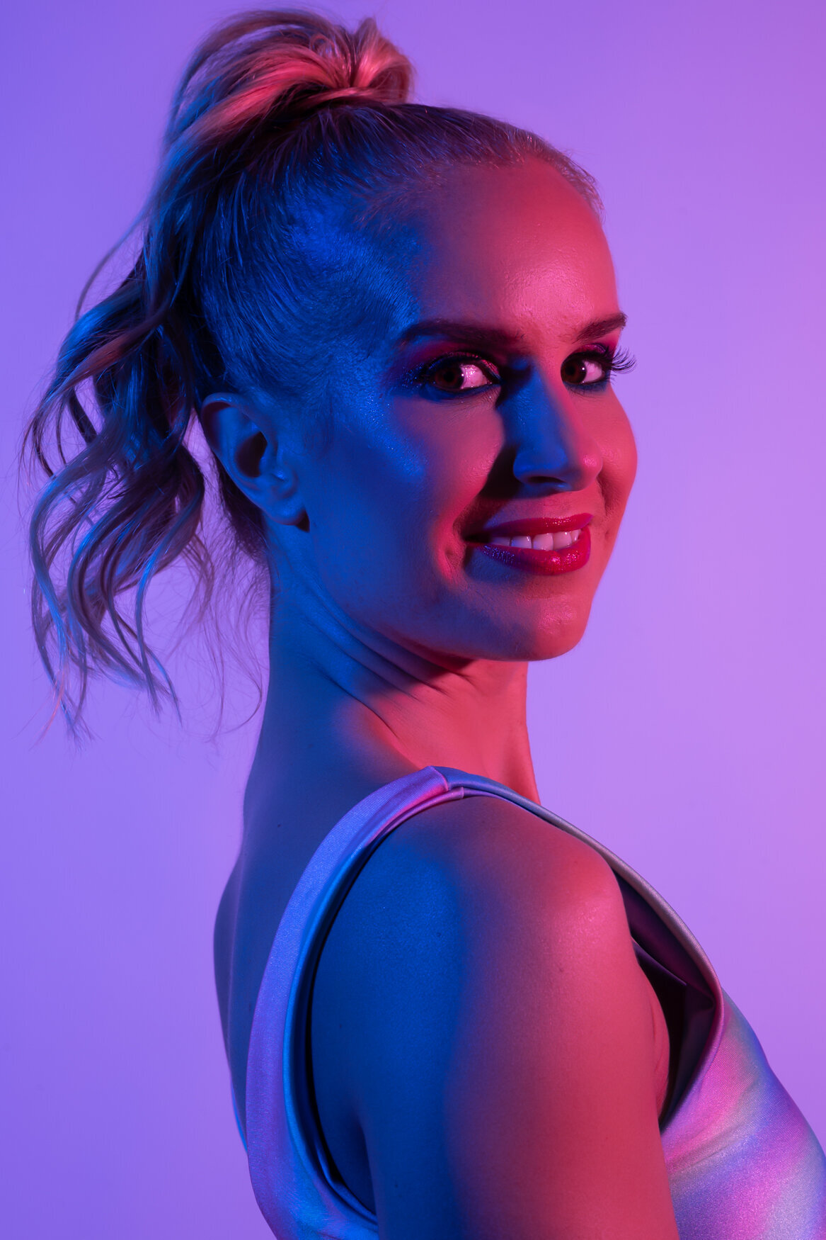 a headshot of a woman wearing a ponytail iluminate by blue and pink lights