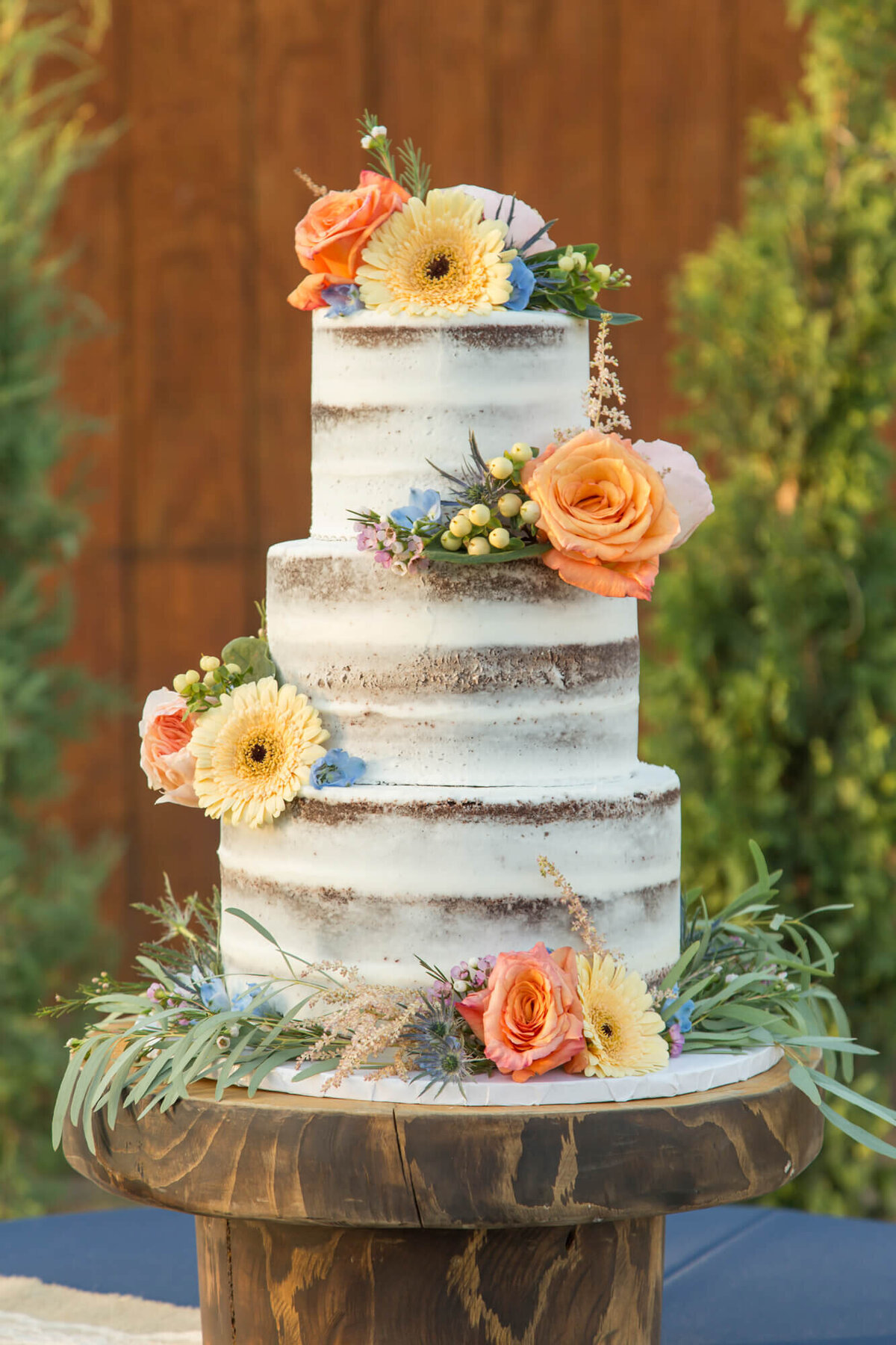 white three tiered wedding cake with colorful flower details at beautiful sunset reception