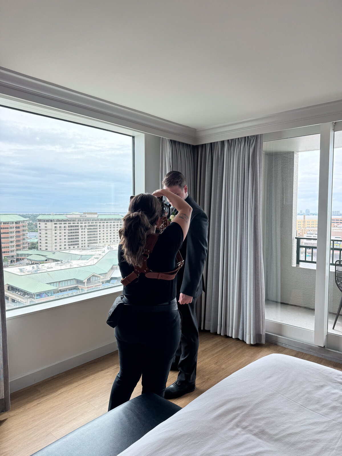 Florida Wedding photographer capturing a groom holding his bride by a large window with a cityscape view at a hotel in Tampa, Florida.