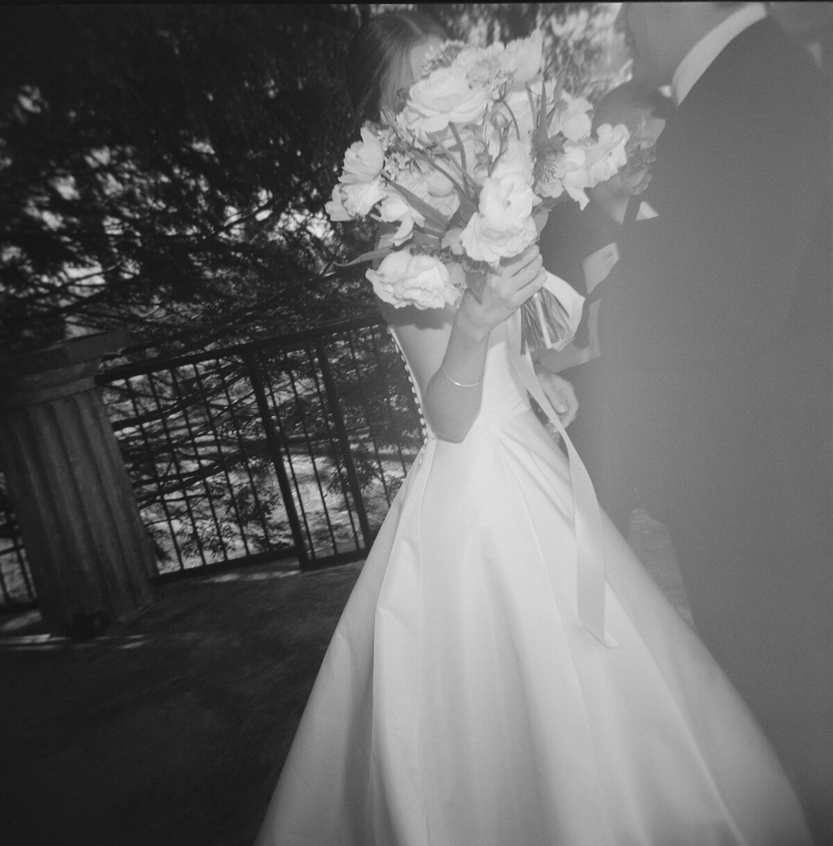 Black and white film photograph of the bride holding her bouquet in front of her face while standing beside the groom at Burritt on the Mountain in Huntsville, Alabama, captured by Perry Hancock.