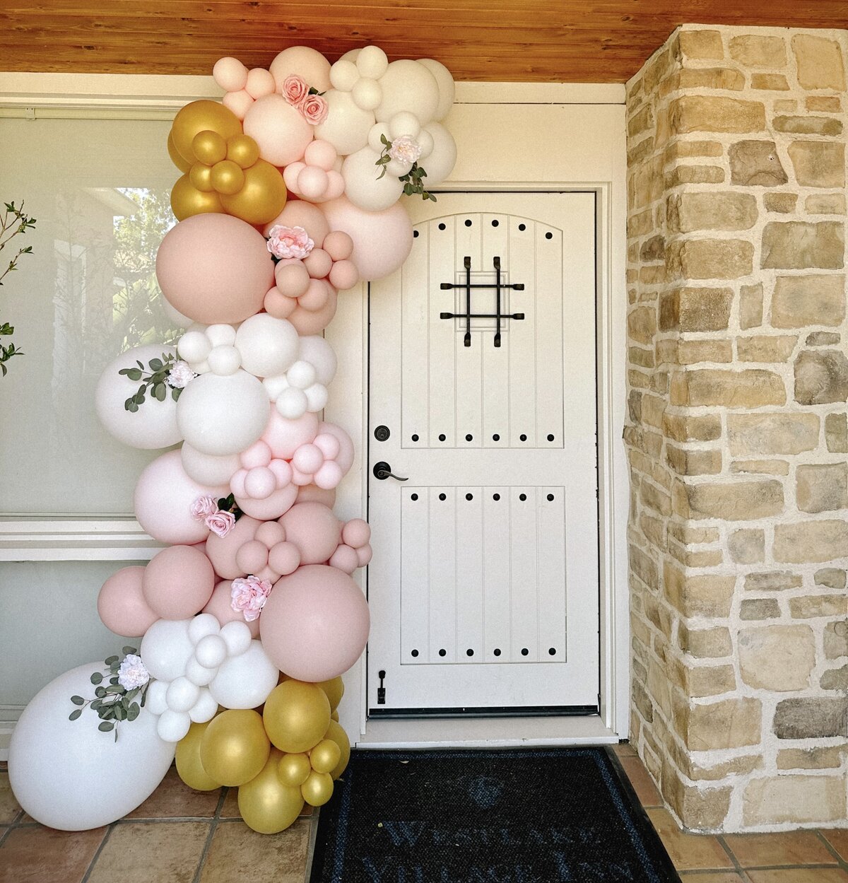 Pink, white and gold balloon arch decorated with greenery around a door