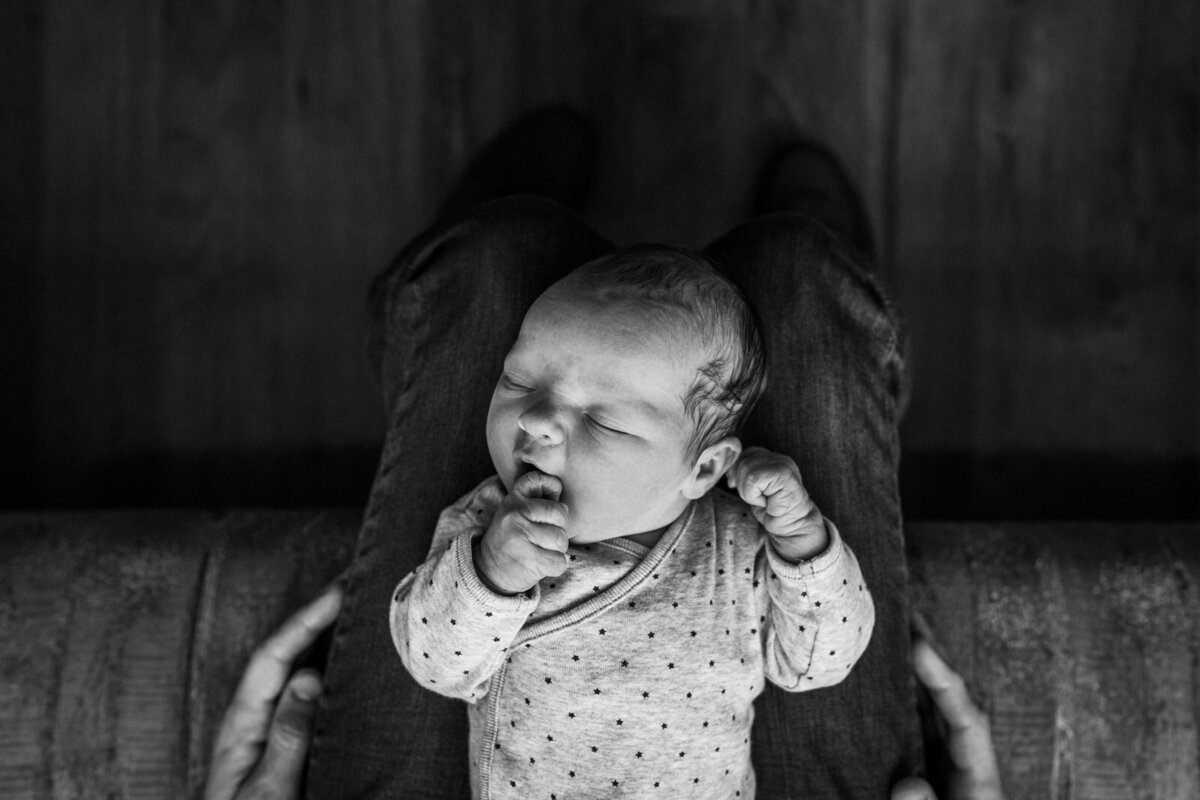 birds-eye view of newborn laying on dad's legs in hospital