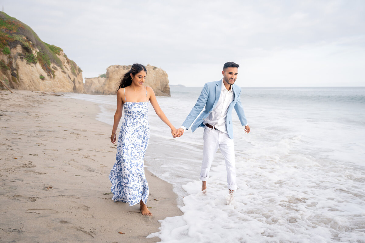 Indian couple eloping at El Matador State Beach in Malibu during low-tide sunset walking on beach.