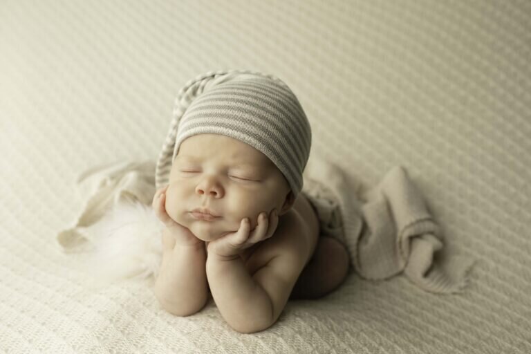 Newborn baby boy posed in the classic froggy position, wearing a soft and cozy sleepy hat, peacefully resting in a dreamy and serene setting