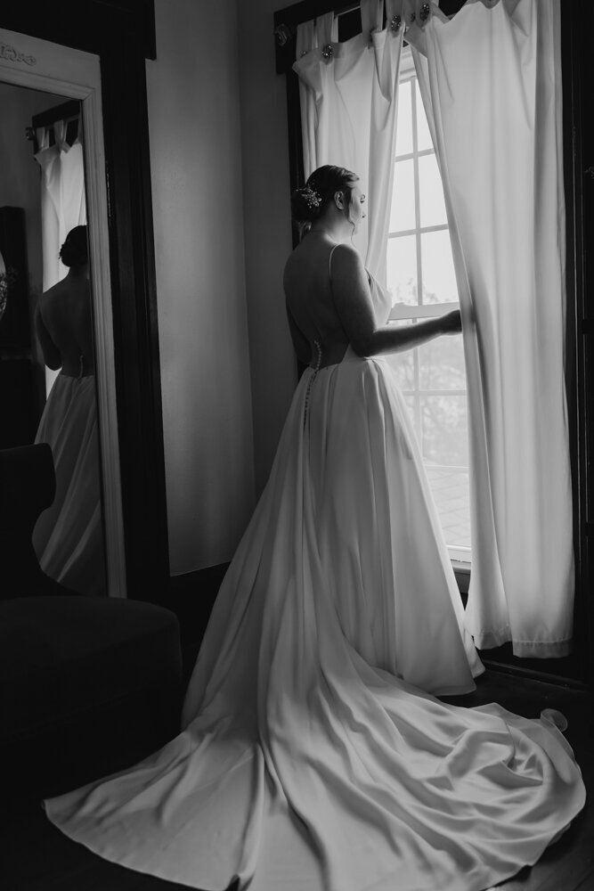 storyteller-collective-photo-co-bride-looking-out-window-in-wedding-dress-sister-hill-manchester-iowa