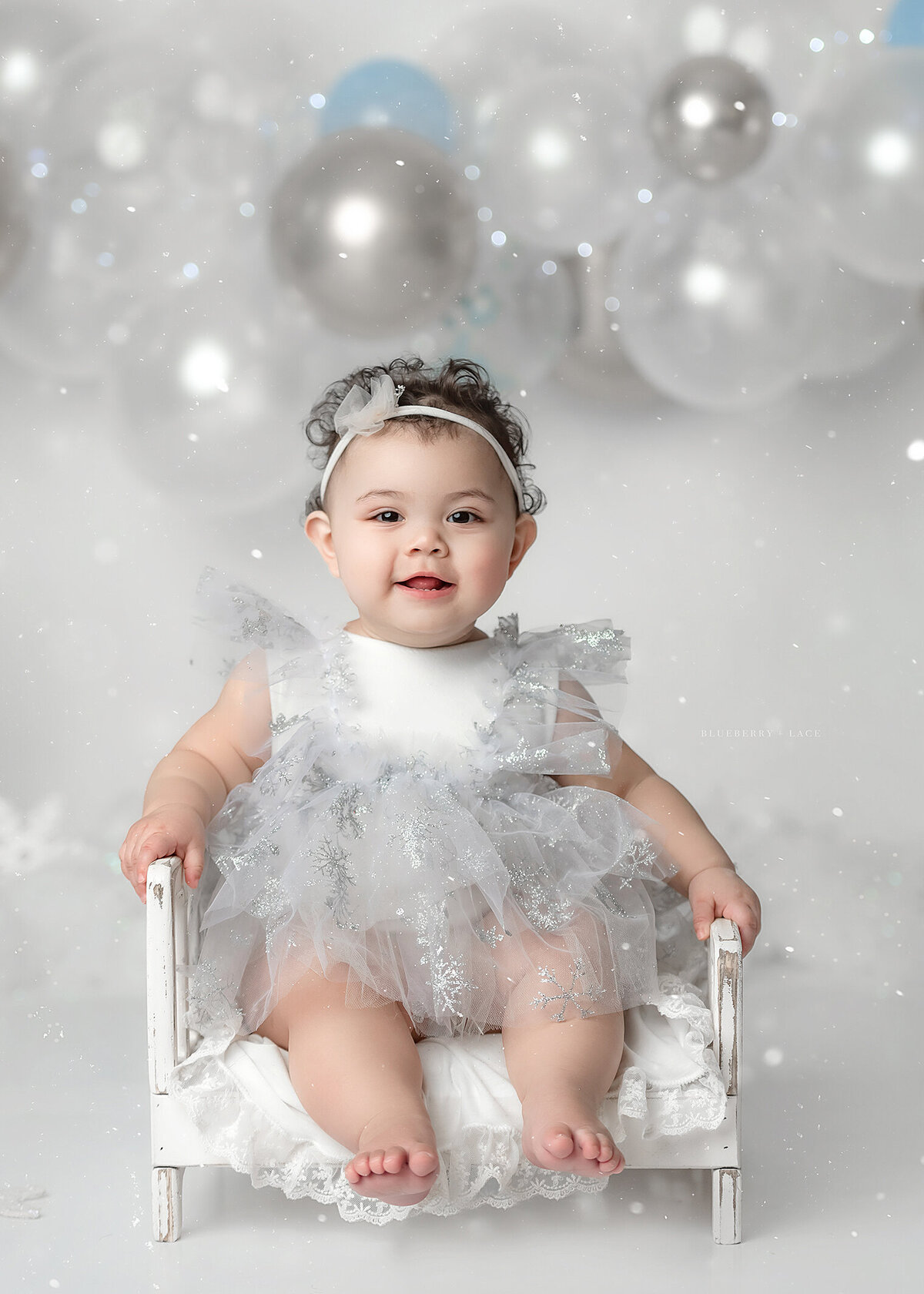 sweet baby girl having her first birthday photo taken from a photographer near me in Oswego sitting on a bed snowflake themed
