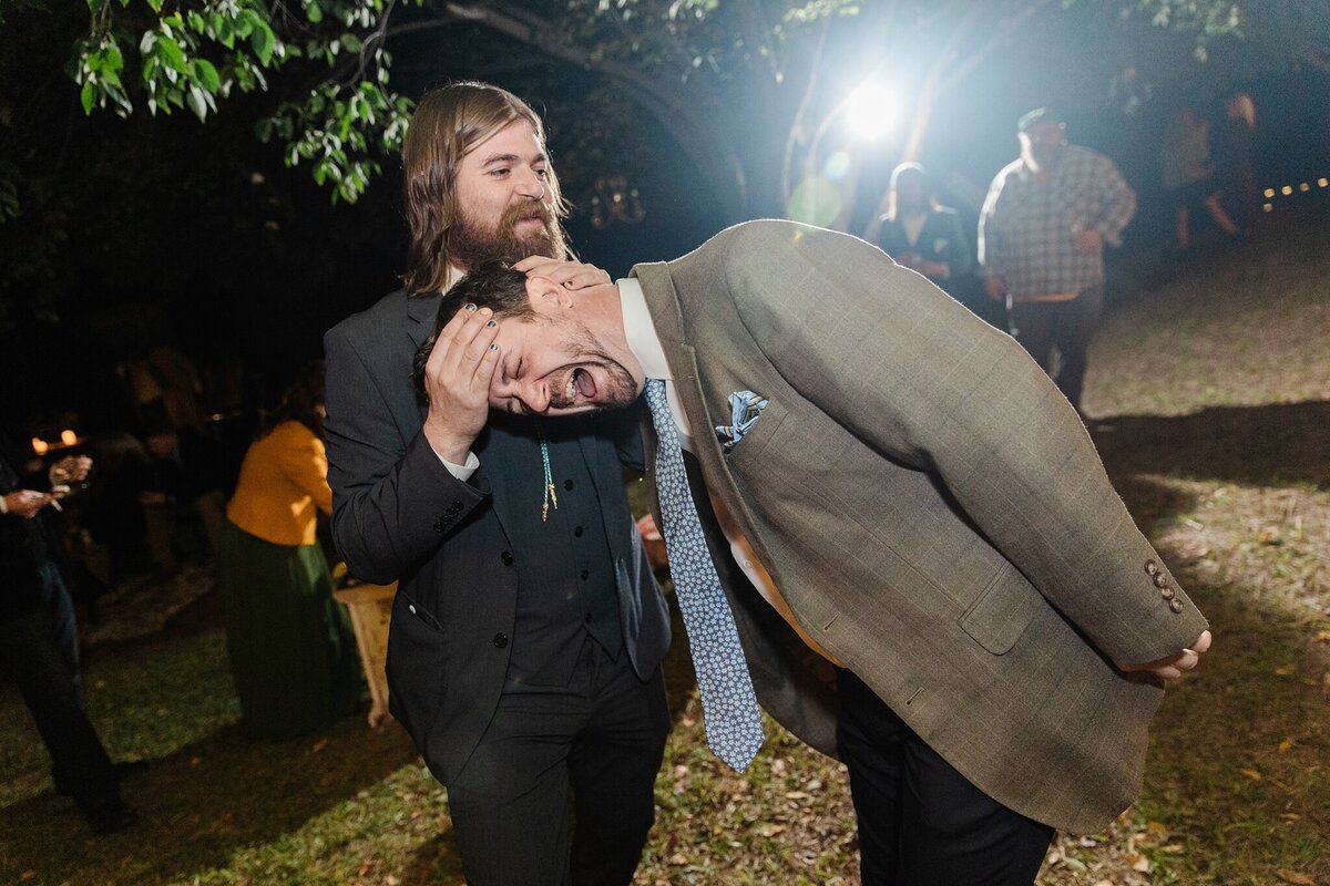 Photo of a groomsman and a wedding guest goofing off and having fun during a wedding reception in Fort Worth, Texas. They are both wearing suits and the groomsman holds the wedding guests's head in his hands.