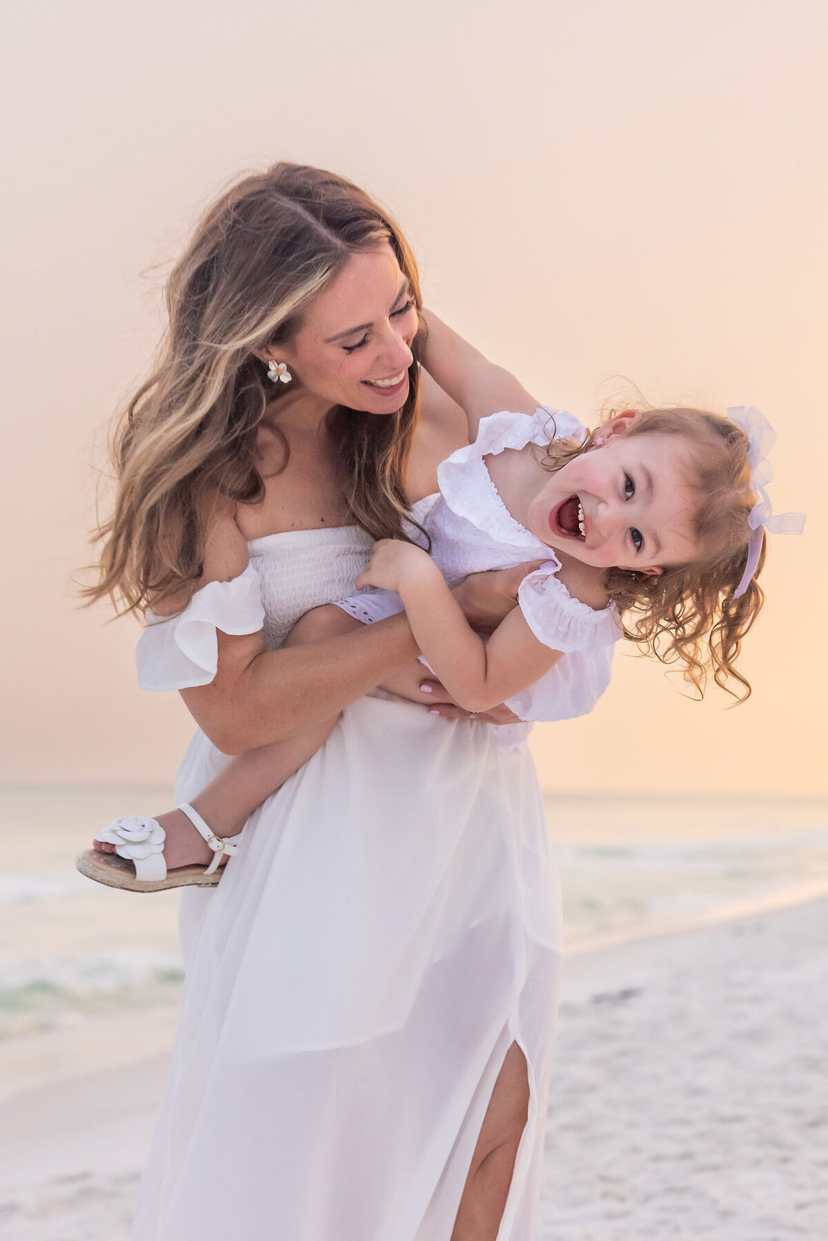 mother leaning forward being playful with toddler daughter on beach in Miramar Beach, Florida.