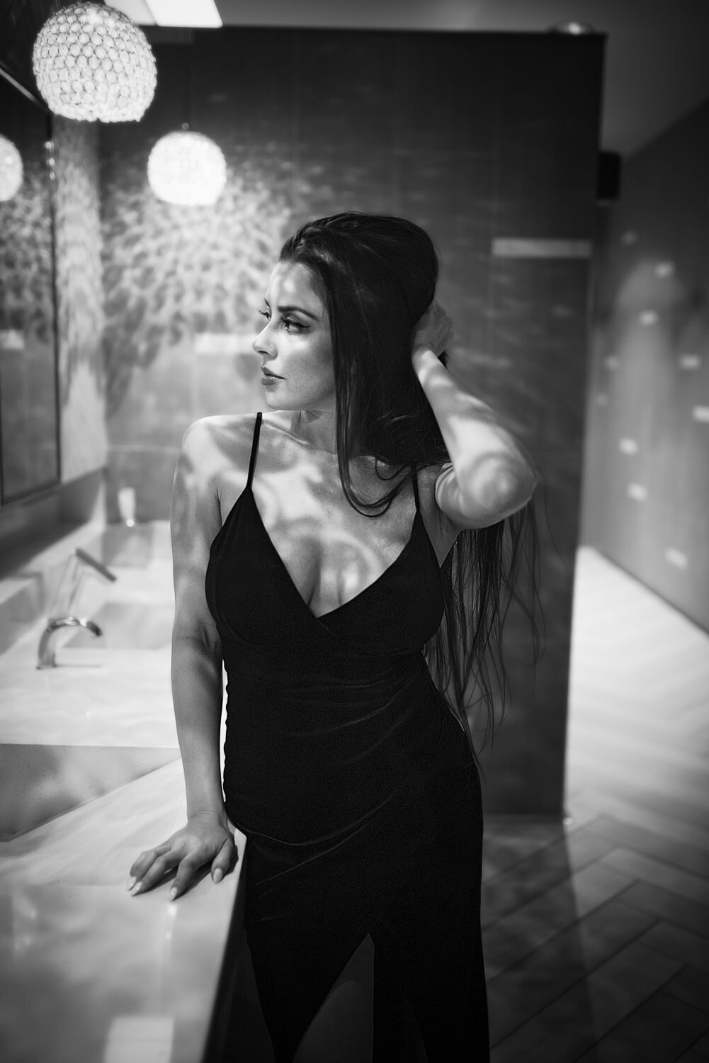Editorial-style portrait of a woman in a cocktail dress looking at herself in the mirror of a chic hotel bathroom.
