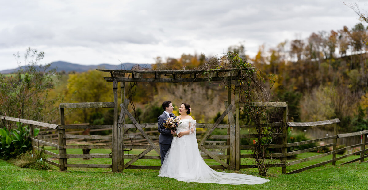 A wedding couple standing in a field with a wooden arch behind them.