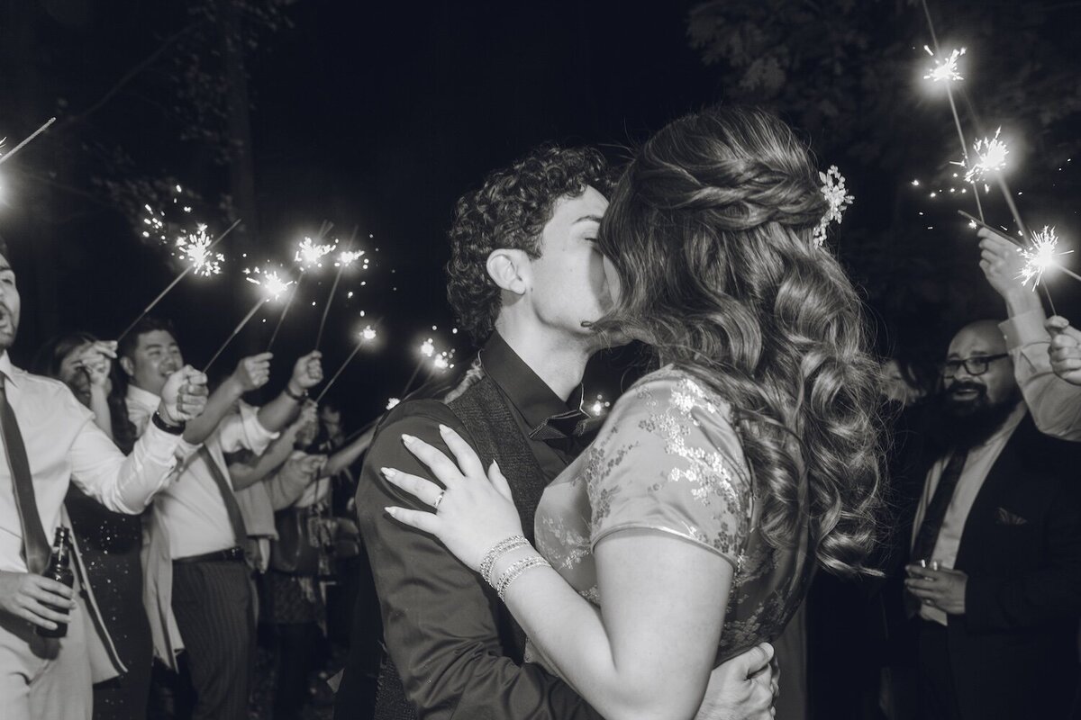 Black and white photo of the newlyweds kissing during a sparkler exit.