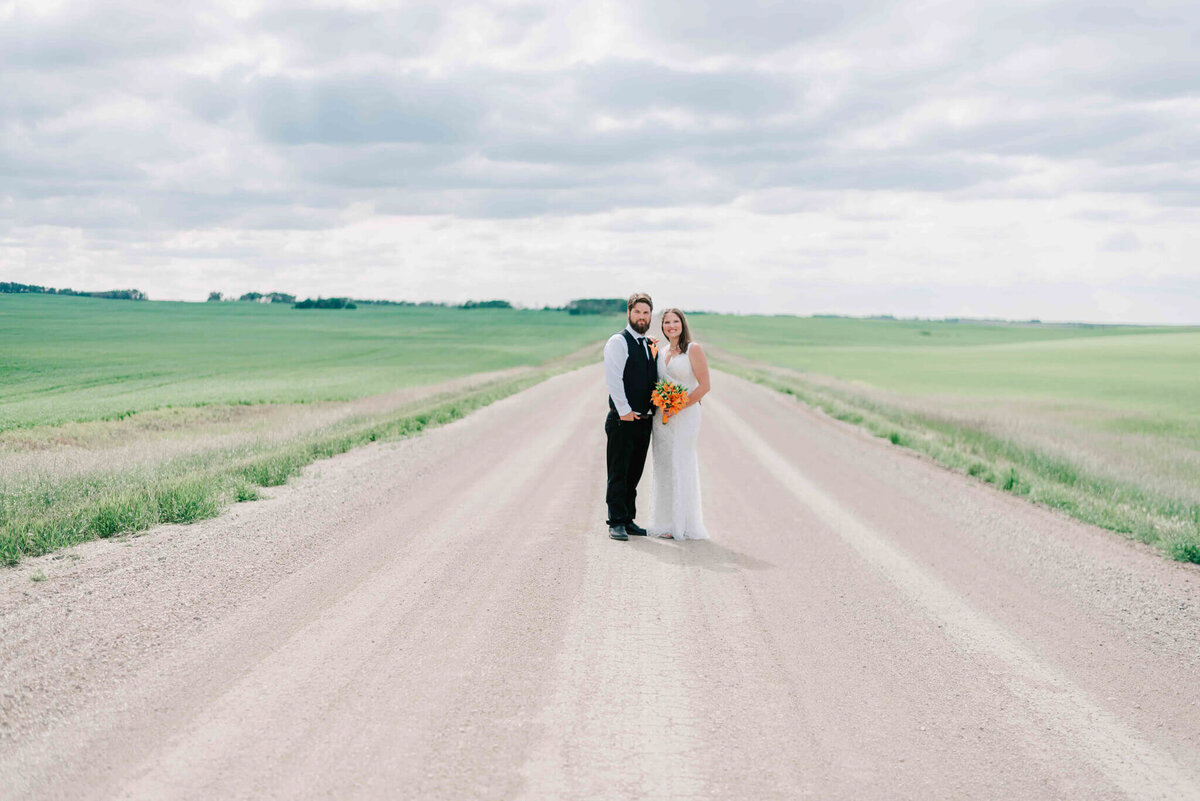 A far away portrait of bride and groom standing close on a gravel road.