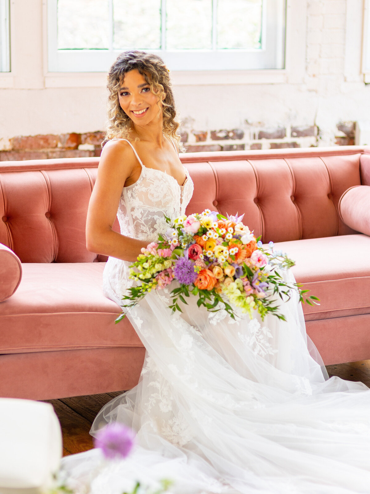 Bride sitting on pink velvet couch with wedding bouquet in hand
