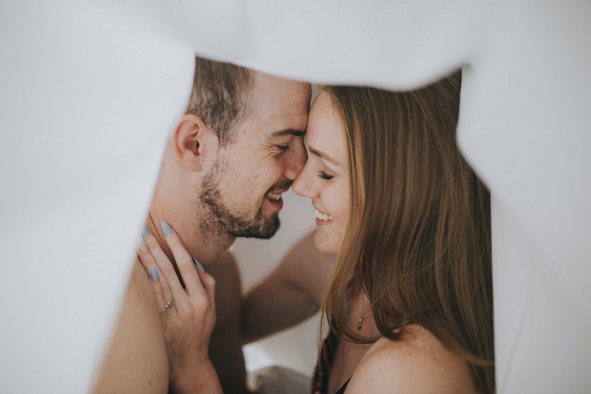 Fun candid couples photo laughing together under sheets in hotel room in Melbourne for Melbourne Hotel Boudoir Couples Photography Session. Sapphire and Stone Photography