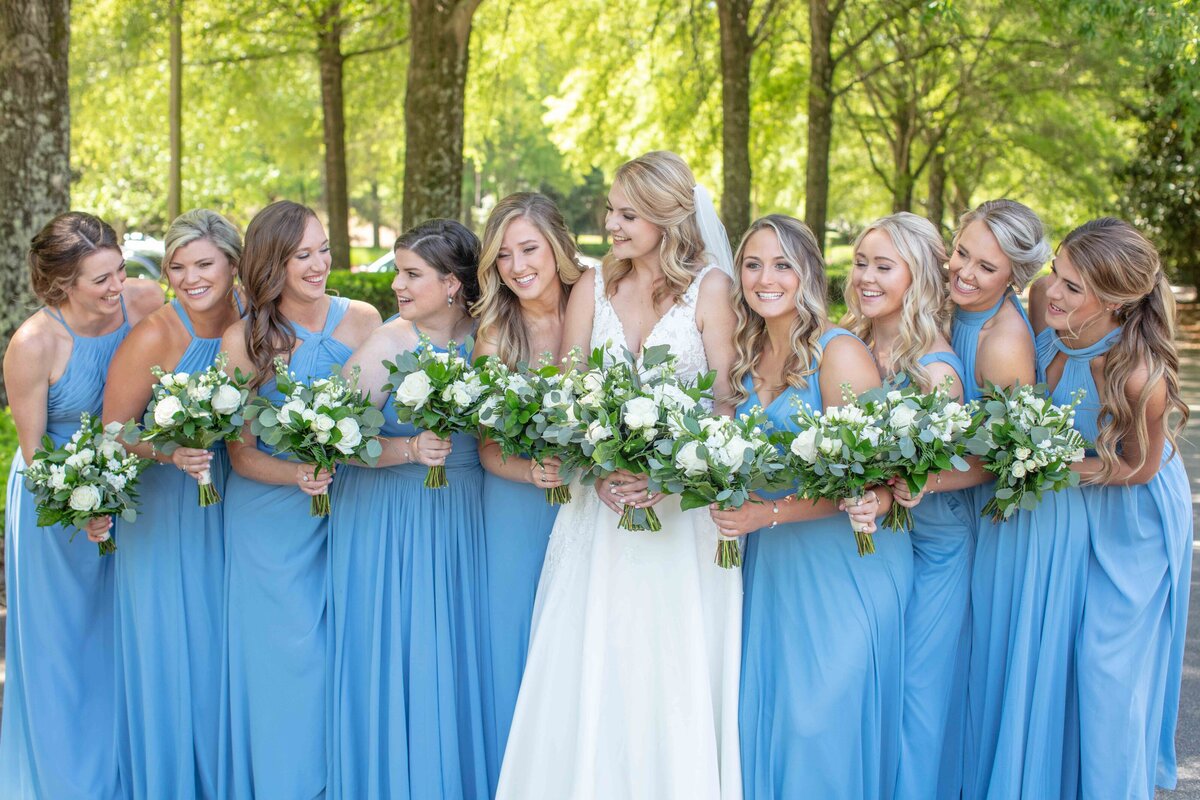 bride surrounded by 9 bridesmaids in periwinkle blue laughing by wedding photographer in Texas