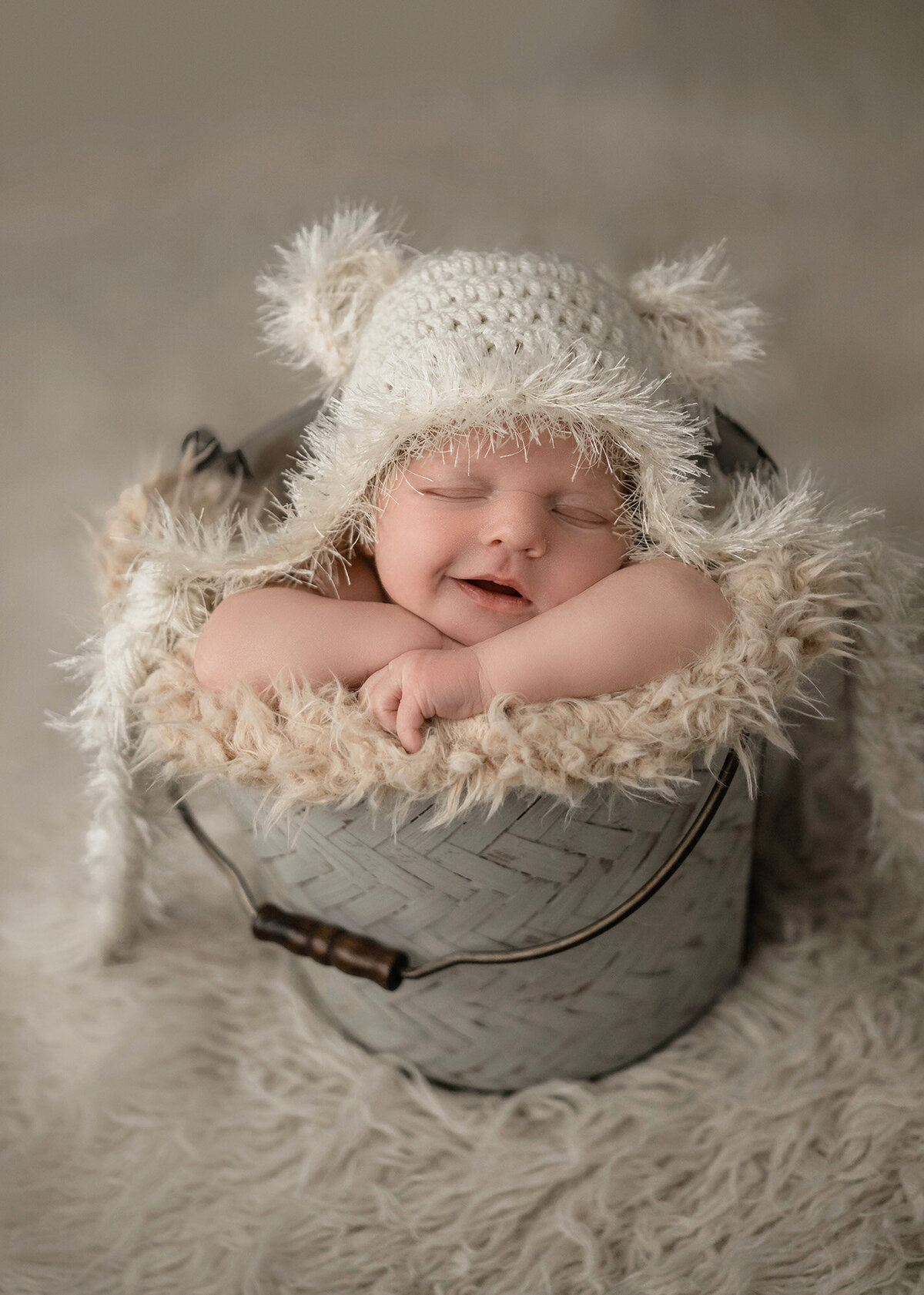 An image from a Pella Newborn Photographer of a newborn baby sleeping in a metal bucket in a white knit bear bonnet