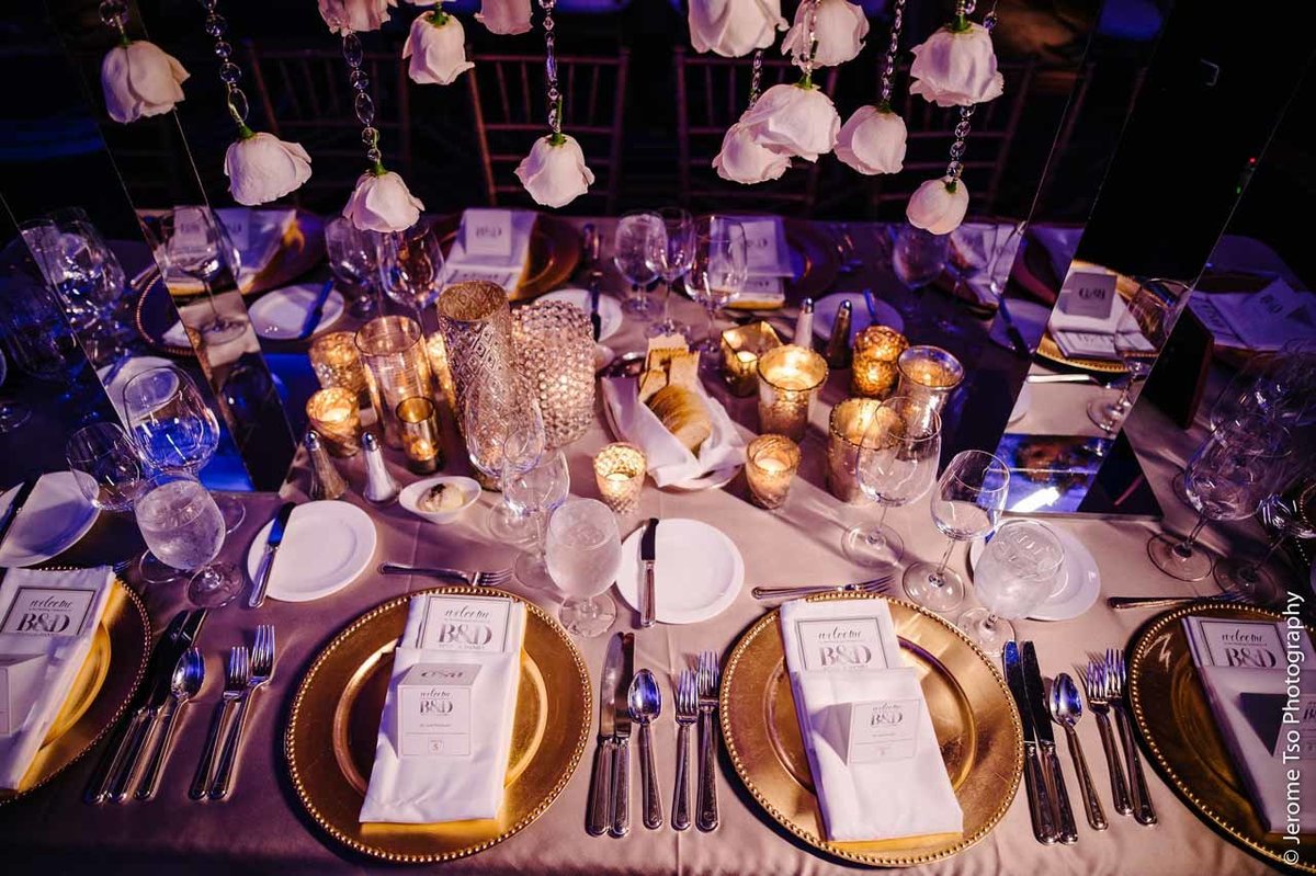 place setting with gold charger plates, gold votive candles, and centerpiece of hanging rose heads