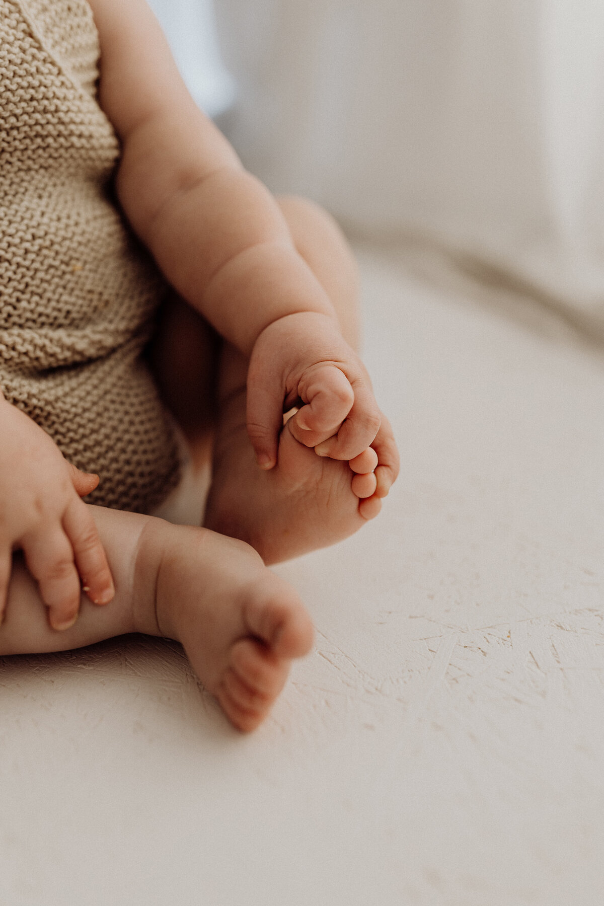 A macro photograph of a baby holding his chubby toes during a photoshoot with lucy jane photography in canterbury