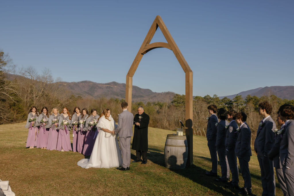 couple eloping to Gatlinburg at Harper's Vineyard with the couple holding hands during their outdoor ceremony surrounded by their bridal party with the Smoky Mountains in the distance