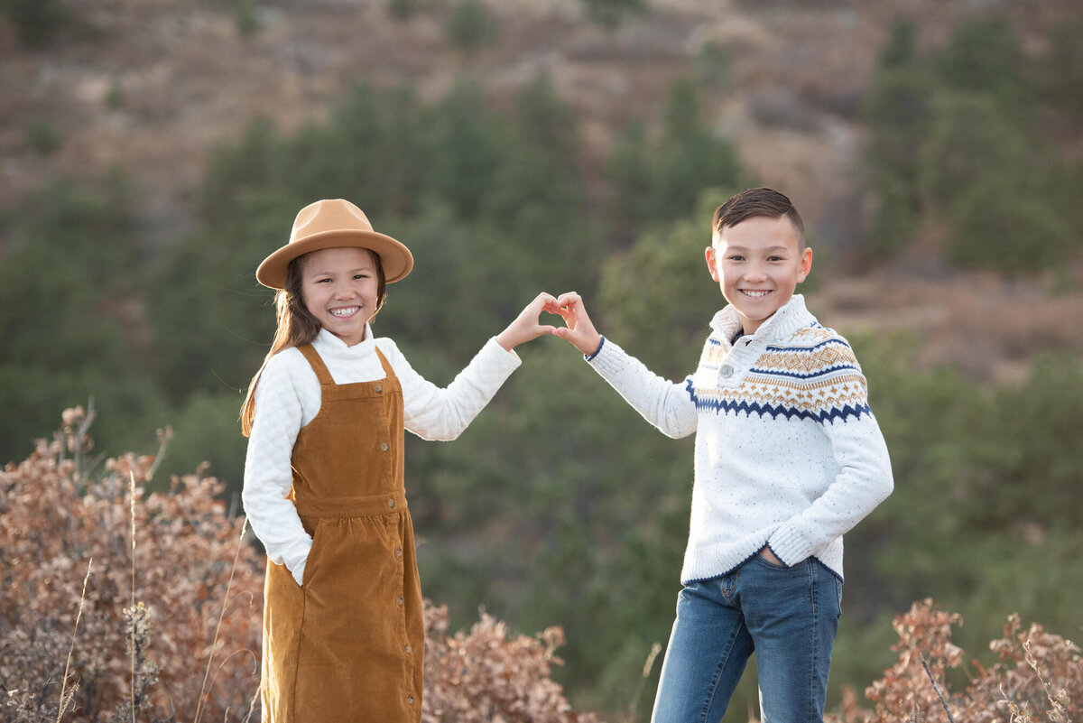 Brother and sister make a heart with their hands while hiking