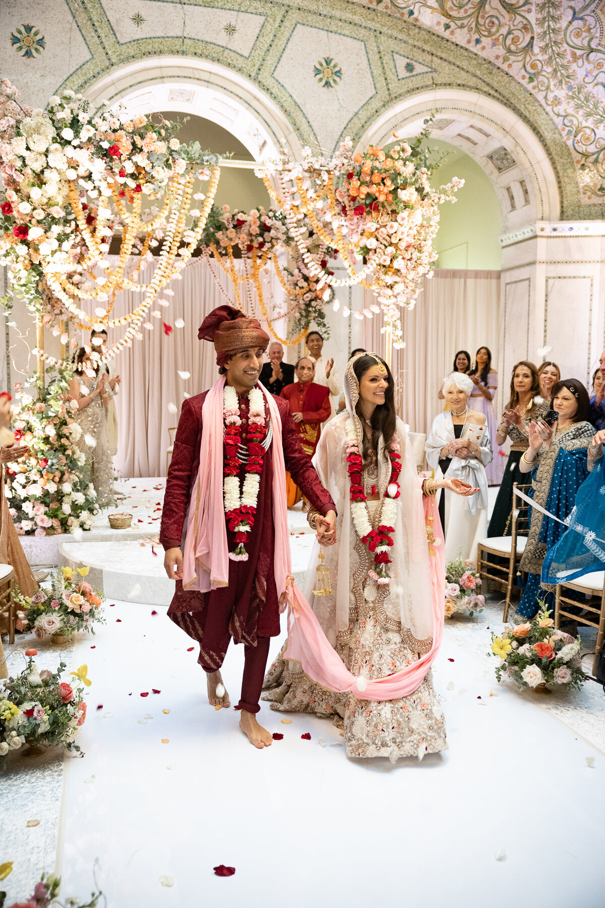 A couple in colorful indian wedding garments recess out of their ceremony as husband and wife