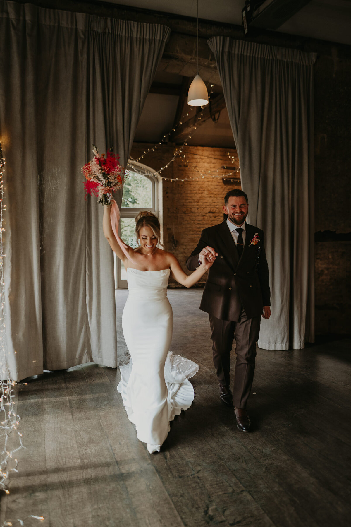 Bride and groom enter the wedding breakfast room at Lapstone Barn to their guests cheering. 