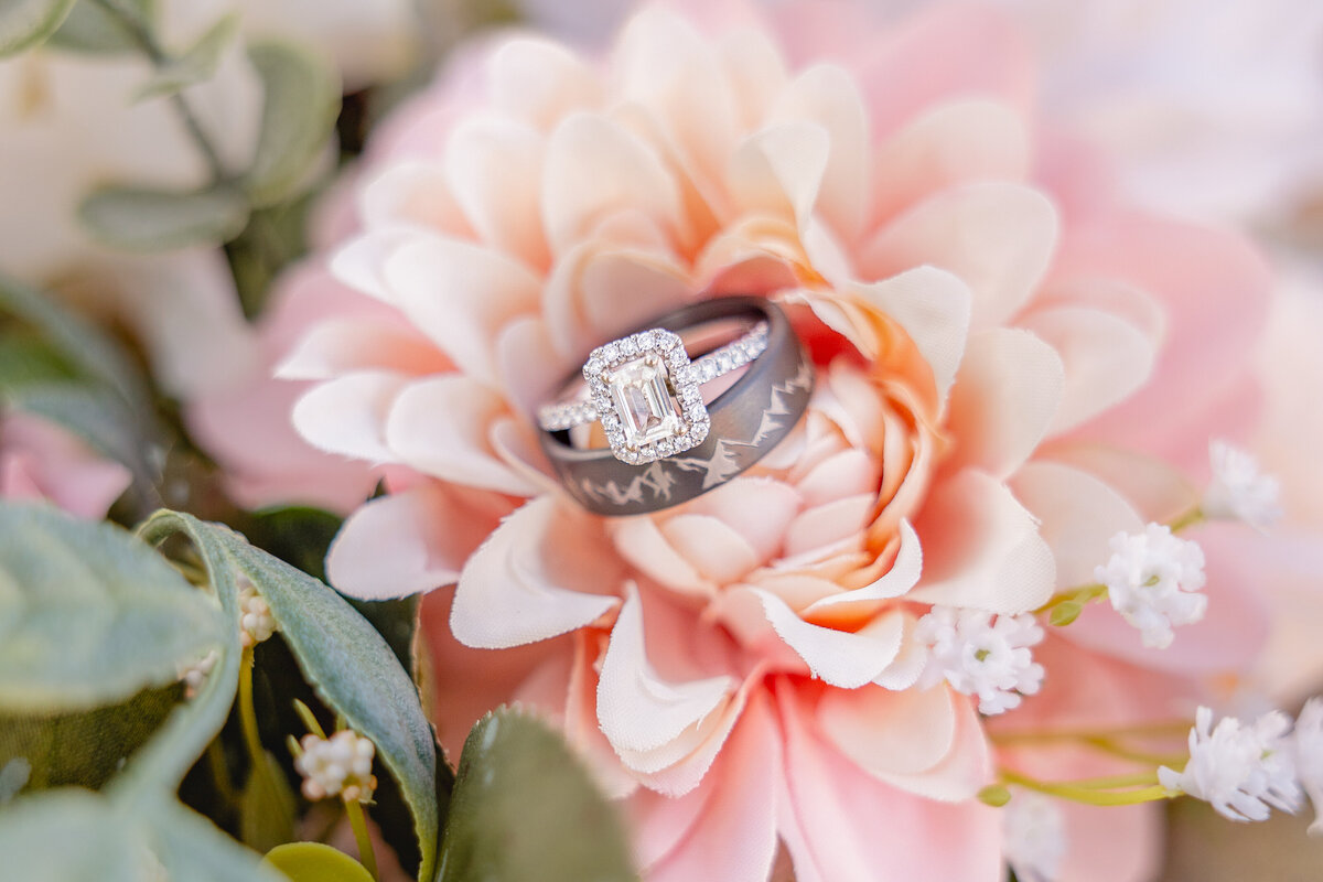 A wedding ring set displayed on pink flowers, surrounded by greenery.