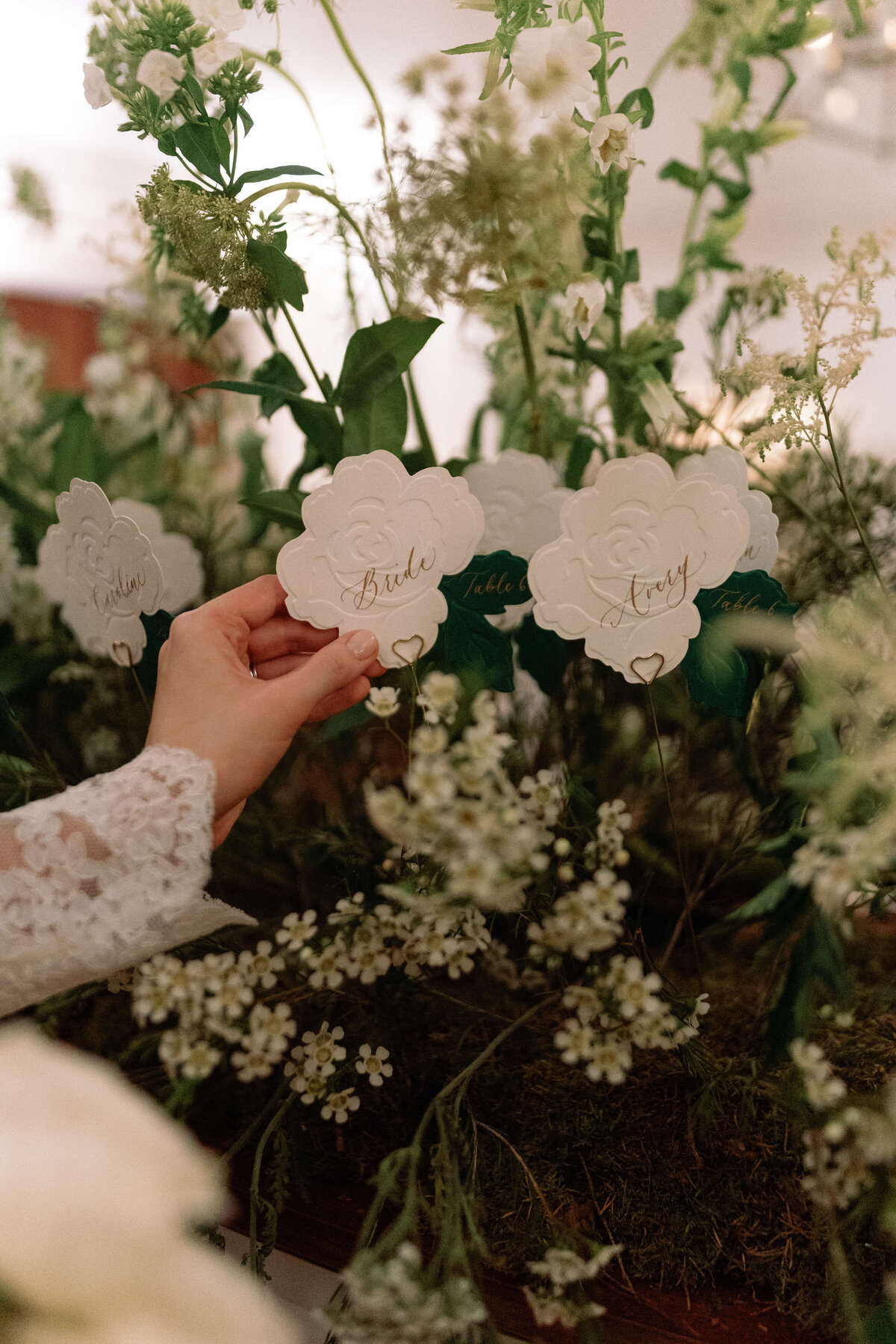 bride picking up her rose shaped paper escort card which is displayed in a meadow of real white and green flowers for a luxury london wedding at the ned